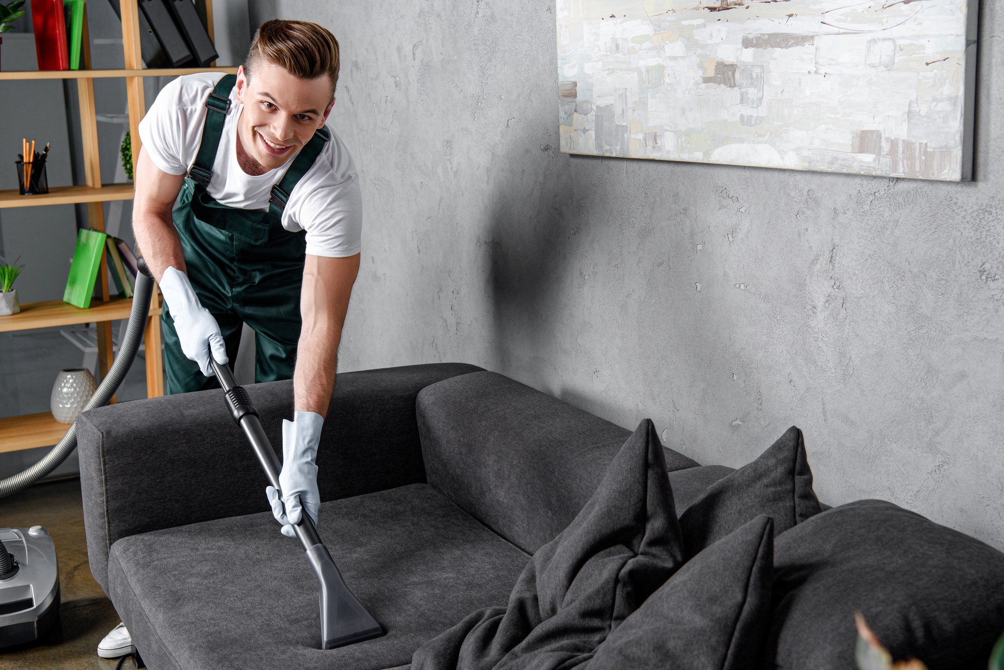 handsome young man in rubber gloves cleaning furniture and smiling at camera